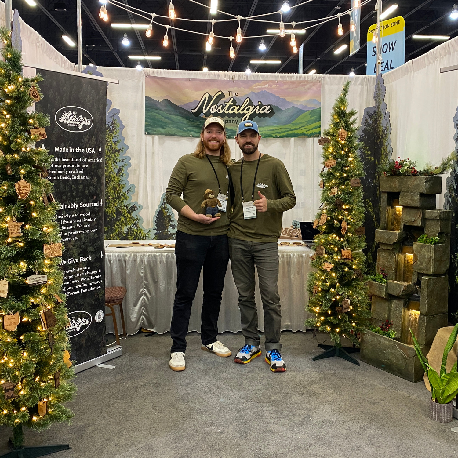 Founders Kevin and Brandon stand in front of christmas trees full of high quality sustainably produced ornaments